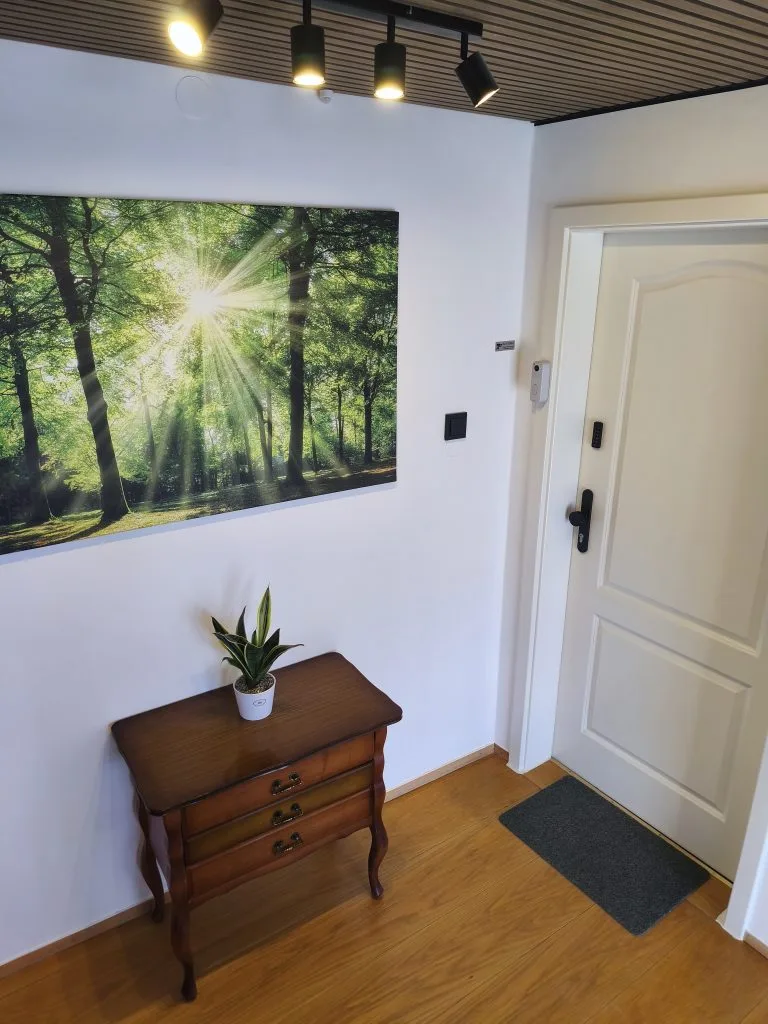 Eingangsbereich der Ferienwohnung Burgperle mit Wohnungstür, Kommode und Waldbild