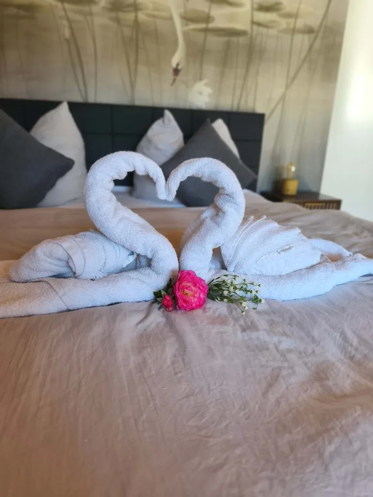 Doppelbett der Ferienwohnung Burgjuwel mit Handtuchschwänen und Blüte unter Holzdecke